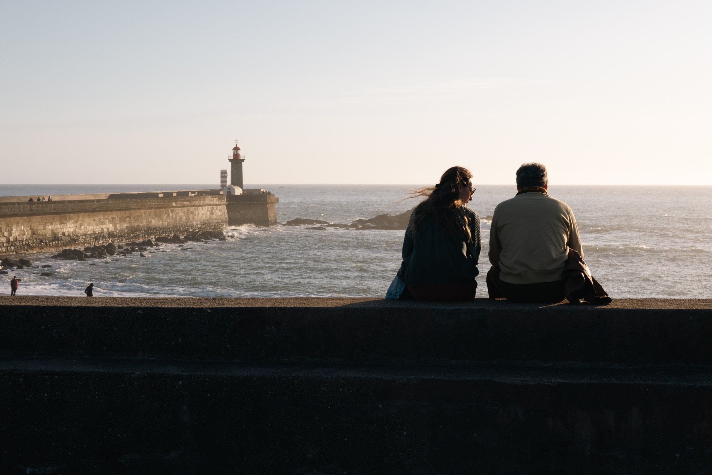 Couple seated by the sea near a lighthouse during warm evening light