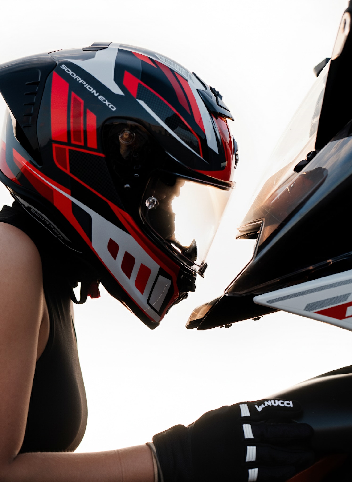 Close portrait of a motorcyclist wearing a red, black and white helmet beside a sport bike