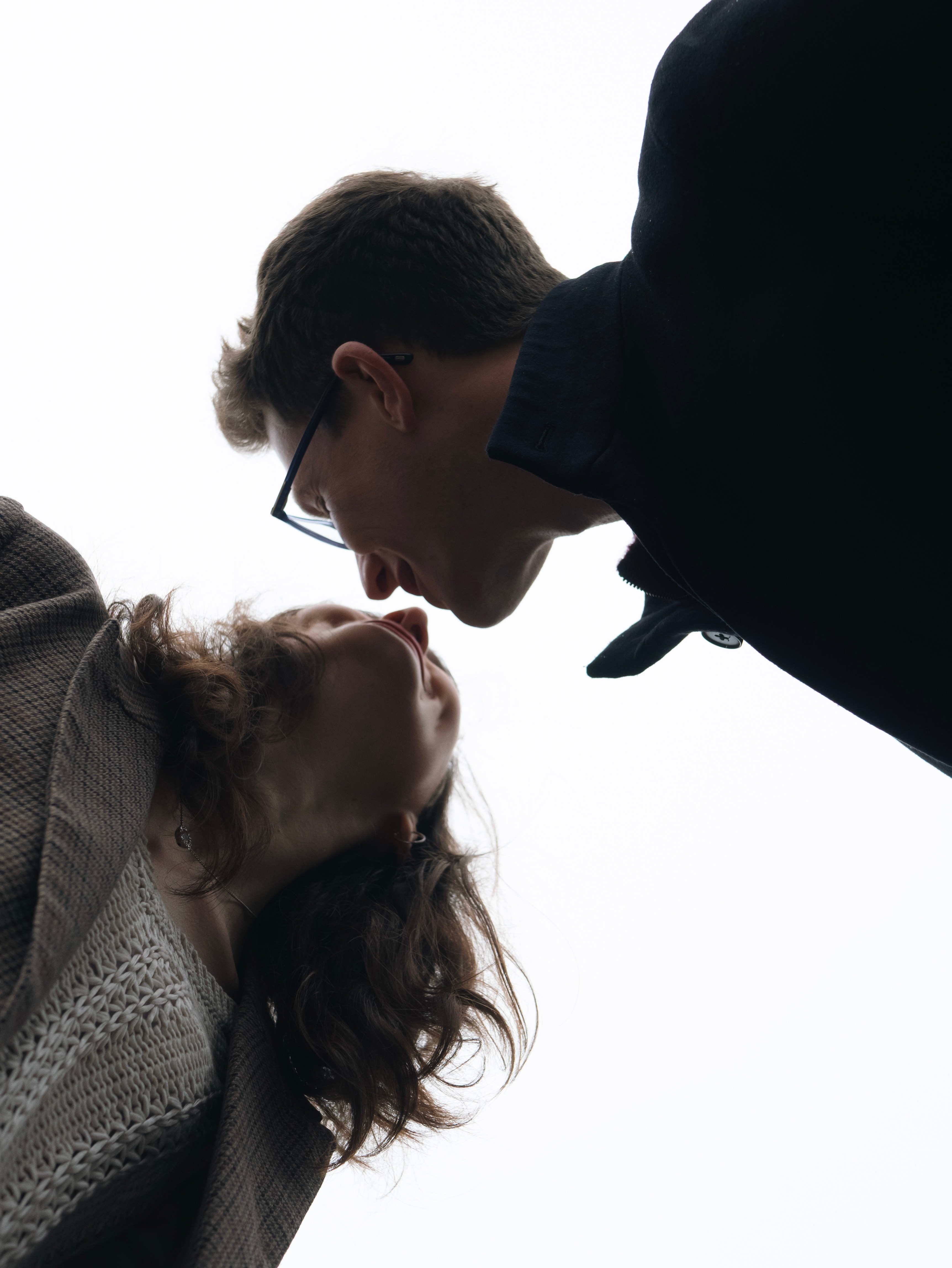 Low-angle portrait of a couple leaning in for a kiss against a bright sky