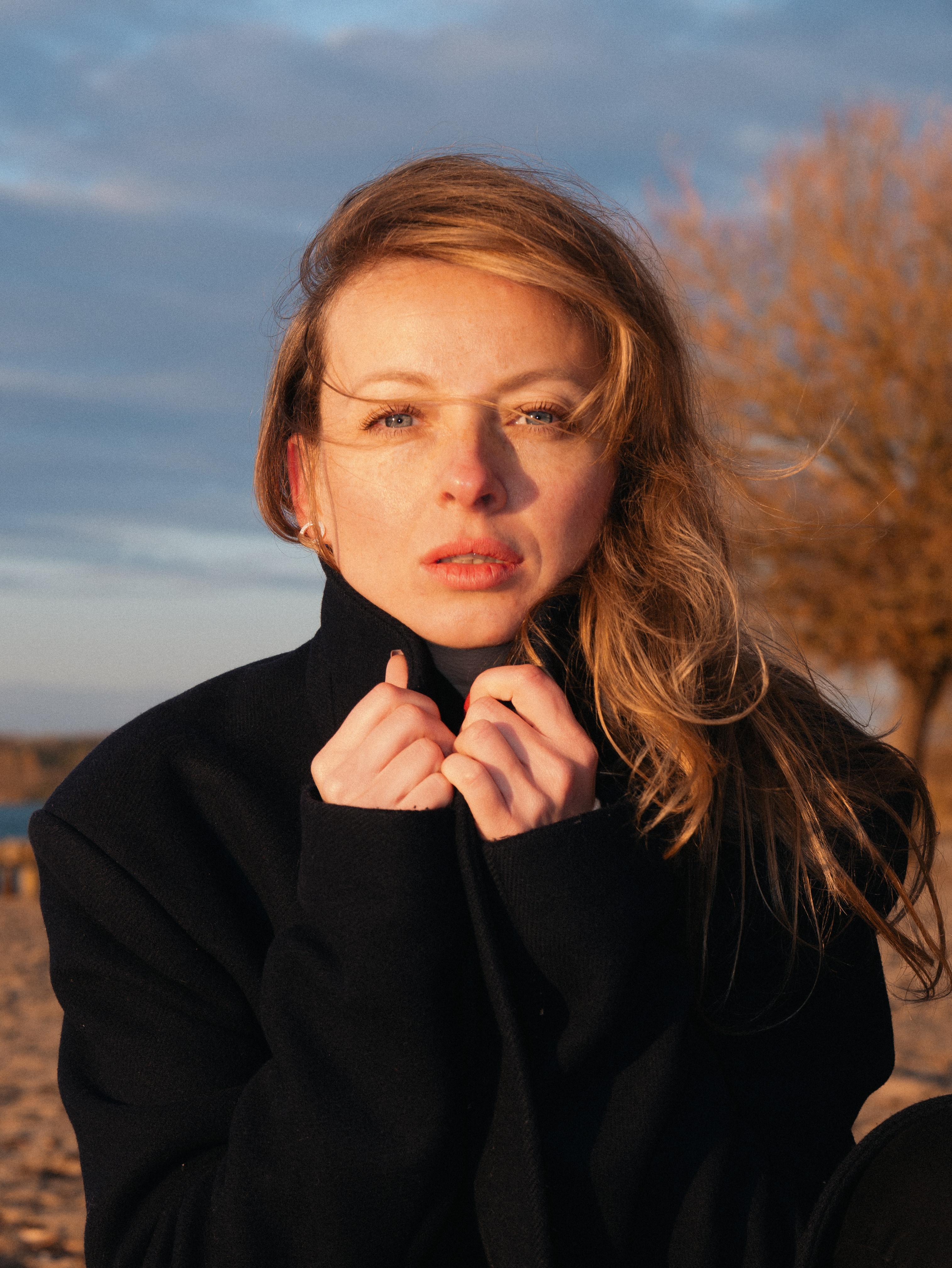 Warm sunset portrait of a woman holding the collar of a black coat near the coast